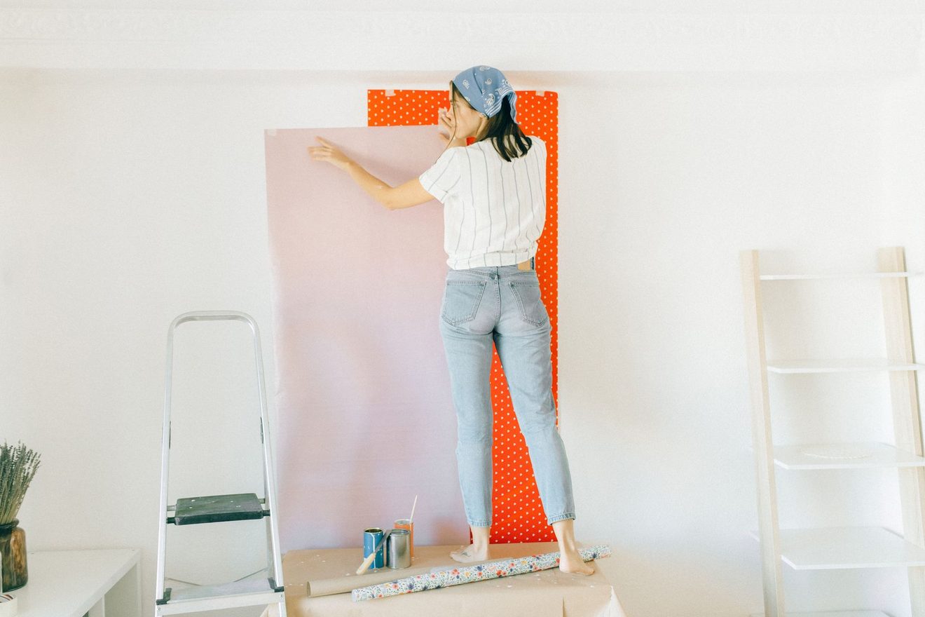 A person on a step smoothing the top of a wallpaper strip
