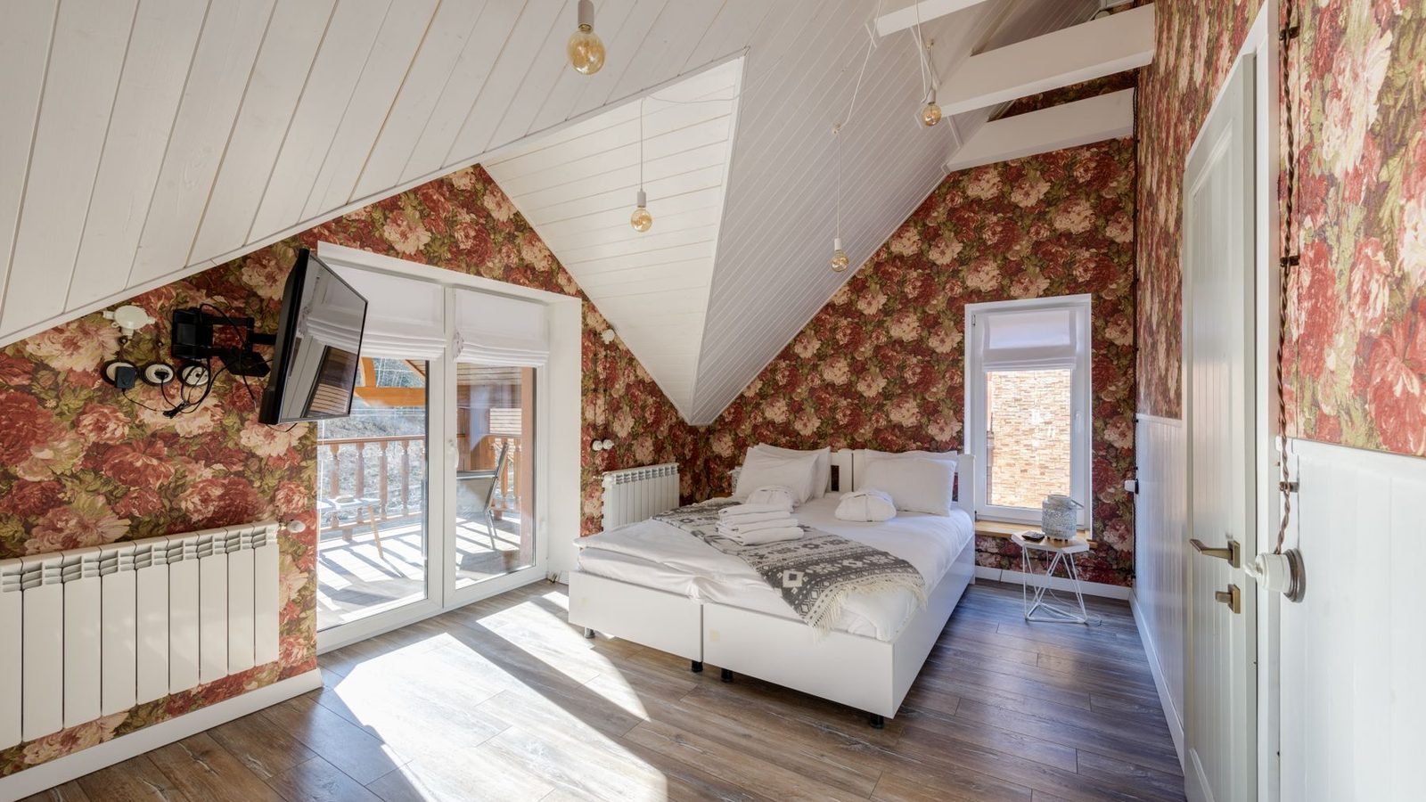 An attic bedroom with a red floral wallpaper covering the sloped walls